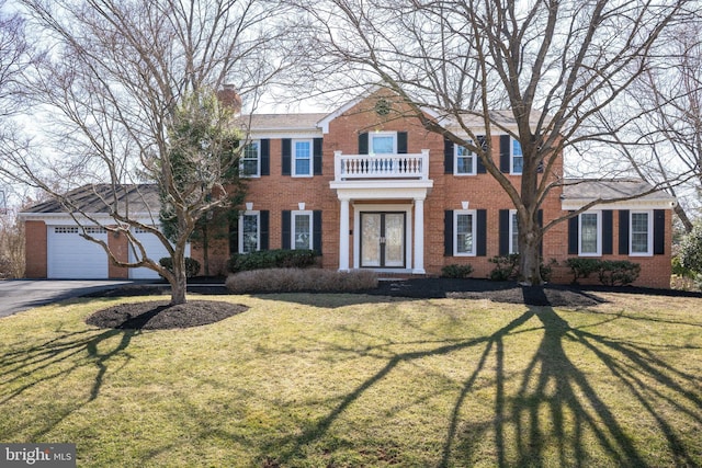 view of front of property featuring a front yard, a balcony, brick siding, and a chimney