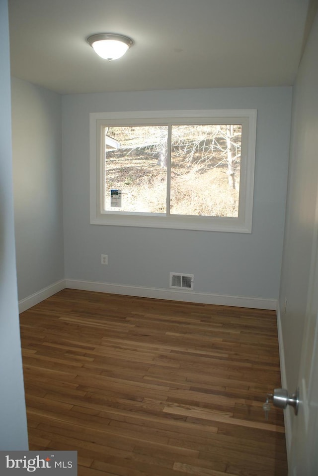 empty room featuring wood finished floors, visible vents, and baseboards