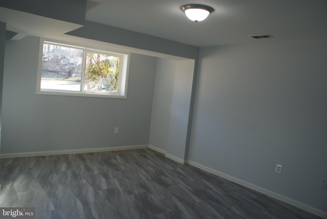 spare room with dark wood-type flooring, visible vents, and baseboards