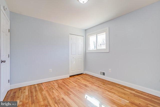 unfurnished bedroom with a closet, baseboards, visible vents, and light wood finished floors