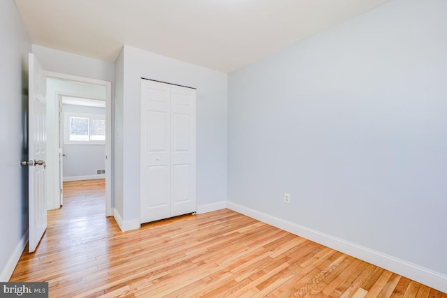 unfurnished bedroom featuring light wood finished floors, a closet, and baseboards