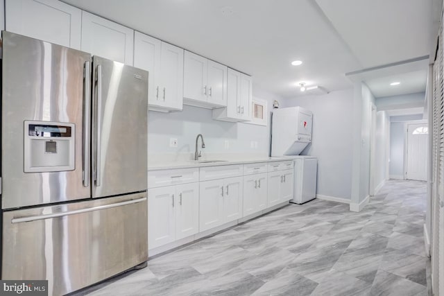 kitchen with stacked washer and clothes dryer, light countertops, white cabinets, a sink, and stainless steel fridge with ice dispenser