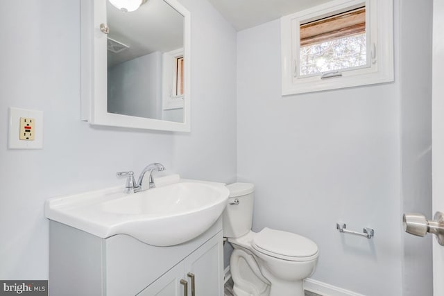 half bathroom with baseboards, visible vents, vanity, and toilet