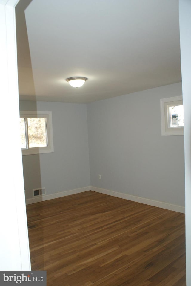 empty room featuring baseboards, visible vents, dark wood-style flooring, and a wealth of natural light