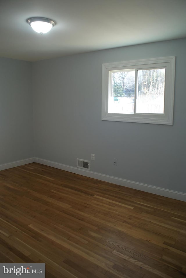 spare room with dark wood-style floors, baseboards, and visible vents