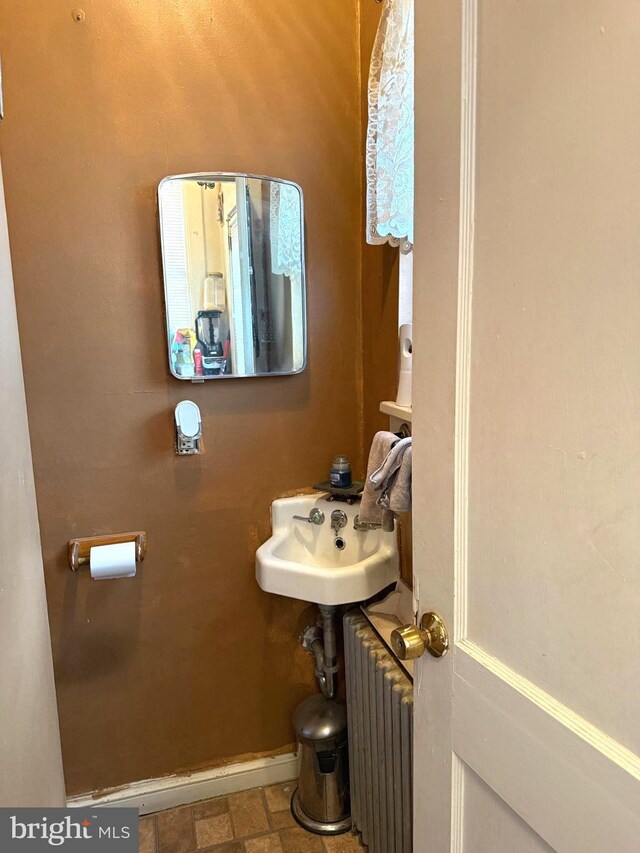 half bath featuring baseboards, a sink, and radiator