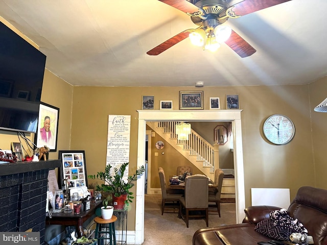 carpeted living area featuring stairs, ceiling fan, and a brick fireplace