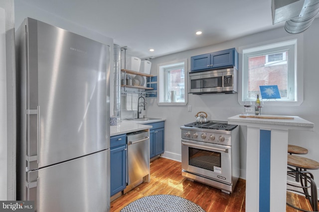 kitchen with blue cabinetry, hardwood / wood-style flooring, sink, appliances with stainless steel finishes, and a breakfast bar area