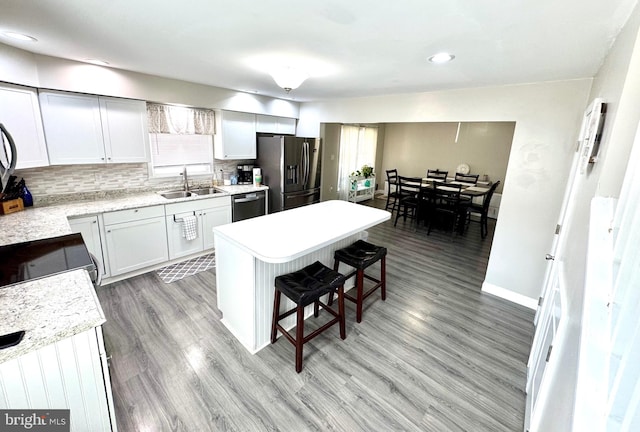 kitchen with stainless steel fridge with ice dispenser, a sink, light countertops, dishwasher, and a kitchen breakfast bar