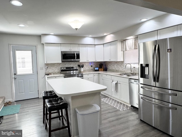 kitchen with a breakfast bar area, light countertops, appliances with stainless steel finishes, wood finished floors, and a sink