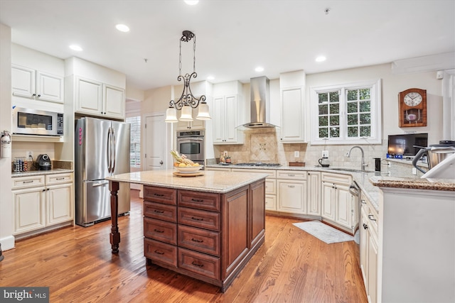 kitchen featuring light wood-style flooring, a sink, stainless steel appliances, wall chimney exhaust hood, and light stone countertops