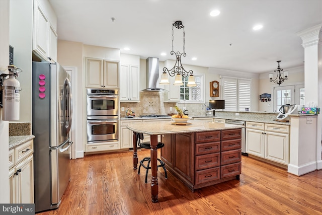 kitchen featuring tasteful backsplash, wall chimney range hood, a kitchen bar, light wood-style flooring, and appliances with stainless steel finishes