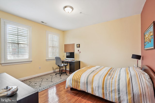 bedroom with wood finished floors, visible vents, and baseboards