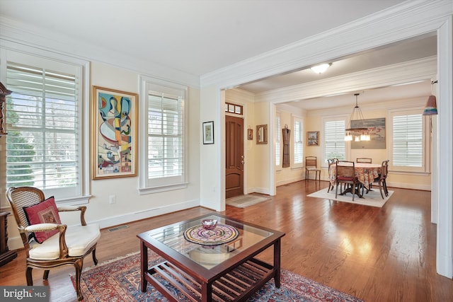 living area with visible vents, crown molding, baseboards, and wood finished floors