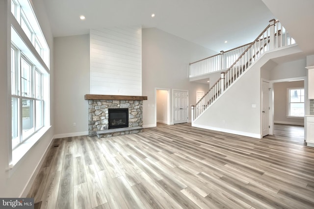 unfurnished living room featuring a high ceiling, a stone fireplace, and light hardwood / wood-style flooring