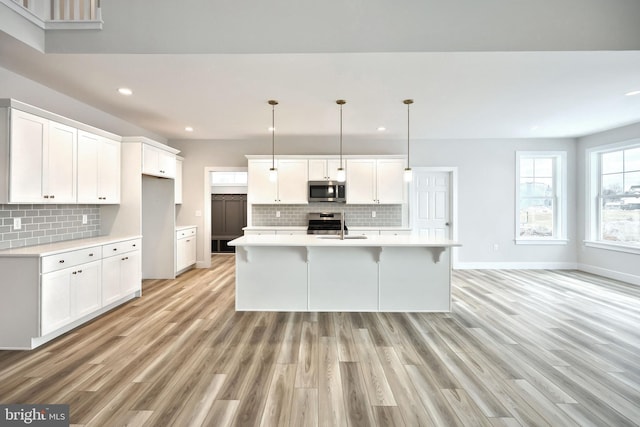 kitchen with white cabinets, appliances with stainless steel finishes, pendant lighting, and a kitchen island with sink