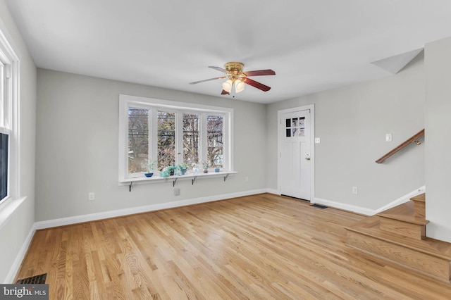 unfurnished living room featuring ceiling fan, visible vents, baseboards, stairway, and light wood finished floors