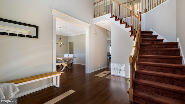 staircase with wood finished floors, visible vents, baseboards, a high ceiling, and ornamental molding