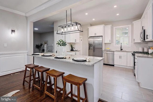 kitchen featuring a kitchen island, white cabinets, stainless steel appliances, and decorative light fixtures