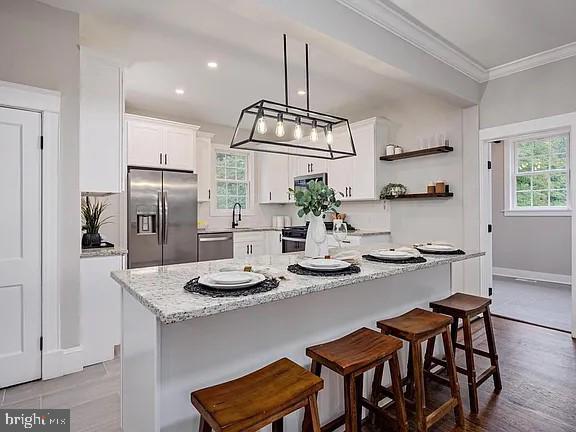 kitchen with appliances with stainless steel finishes, a breakfast bar, a center island, crown molding, and white cabinets