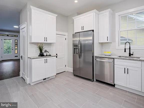 kitchen featuring sink, stainless steel appliances, white cabinets, and light stone counters