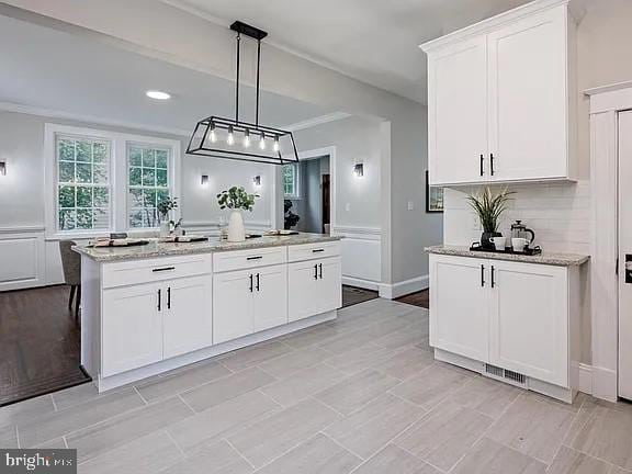 kitchen featuring white cabinets, an island with sink, and hanging light fixtures