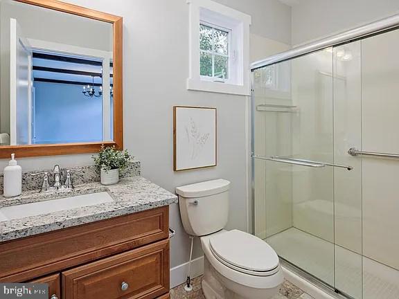 bathroom featuring toilet, vanity, and a shower with shower door