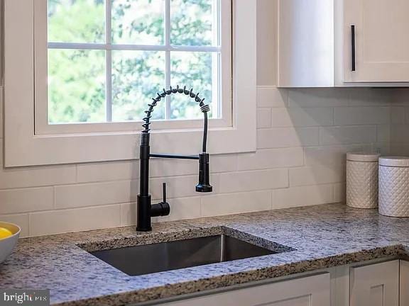 details featuring sink, white cabinets, light stone countertops, and decorative backsplash