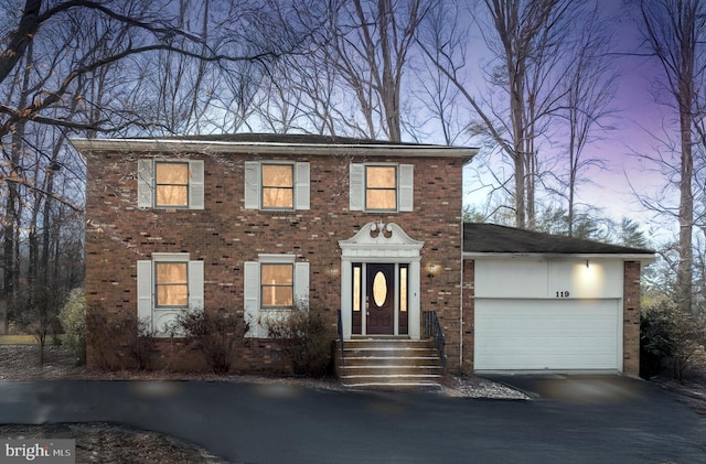 colonial home featuring aphalt driveway, brick siding, and an attached garage