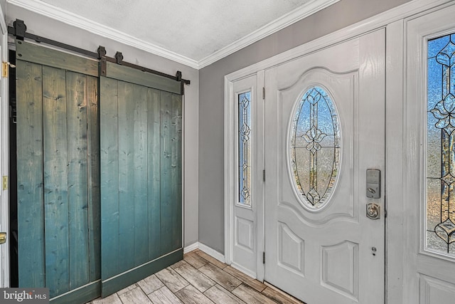 foyer entrance with crown molding, baseboards, a barn door, light wood-style flooring, and a textured ceiling