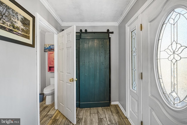 entrance foyer with a textured ceiling, a barn door, ornamental molding, and wood tiled floor