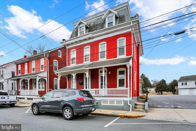 second empire-style home featuring covered porch, a shingled roof, and mansard roof