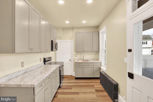 kitchen with stainless steel appliances, a sink, light countertops, gray cabinets, and radiator heating unit