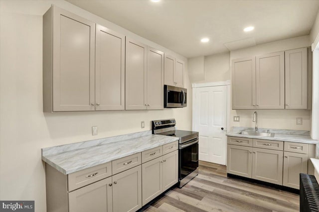 kitchen featuring light wood finished floors, stainless steel appliances, recessed lighting, gray cabinets, and a sink