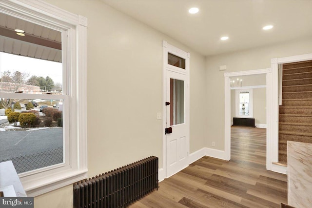 hallway featuring radiator, a healthy amount of sunlight, stairs, and wood finished floors