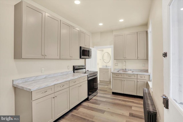 kitchen featuring light wood finished floors, radiator heating unit, stainless steel appliances, a sink, and recessed lighting