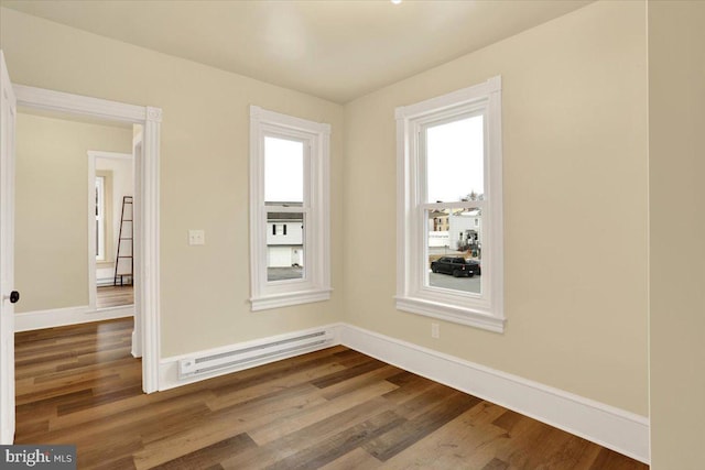 empty room featuring a baseboard heating unit, baseboards, and wood finished floors