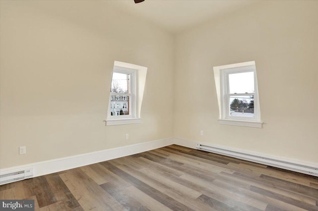 spare room featuring a baseboard radiator, baseboards, a wealth of natural light, and wood finished floors