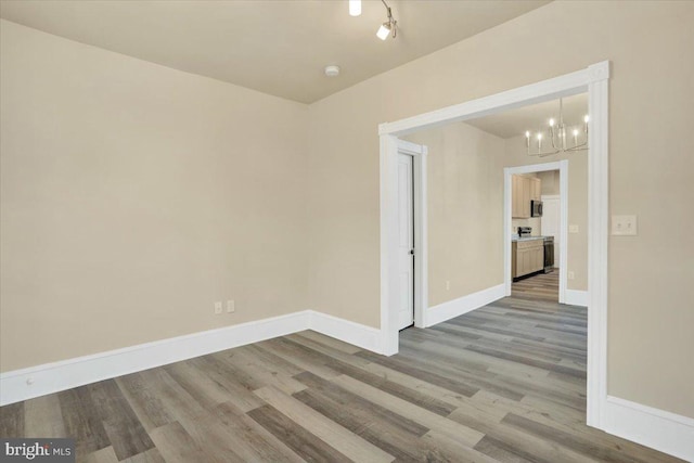 empty room with a notable chandelier, baseboards, and wood finished floors