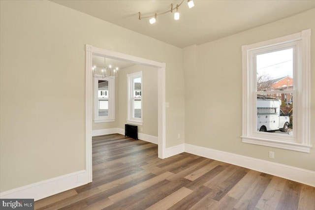 empty room with a chandelier, dark wood-type flooring, and baseboards