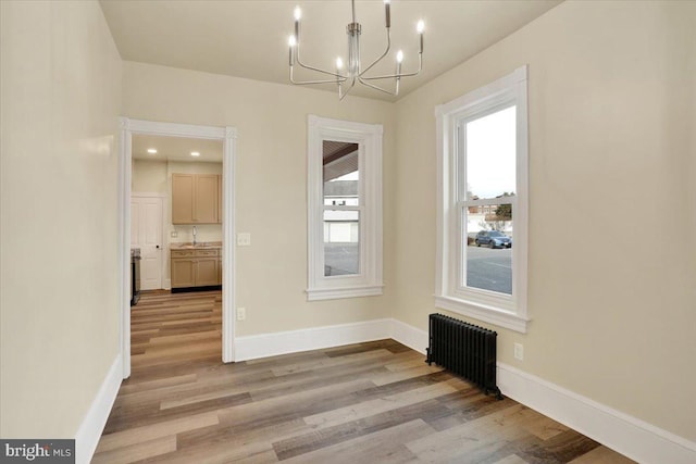 unfurnished dining area with baseboards, radiator heating unit, light wood-style flooring, an inviting chandelier, and a sink