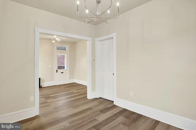 unfurnished dining area with an inviting chandelier, wood finished floors, and baseboards