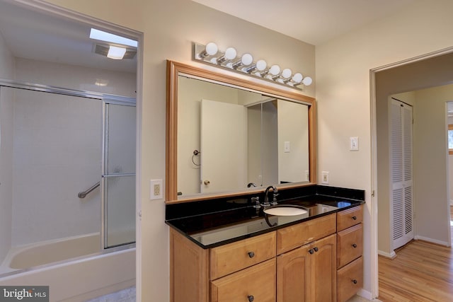 bathroom with visible vents, baseboards, wood finished floors, enclosed tub / shower combo, and vanity