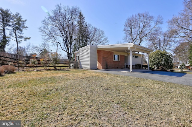 view of side of home featuring an attached carport, fence, driveway, a lawn, and brick siding