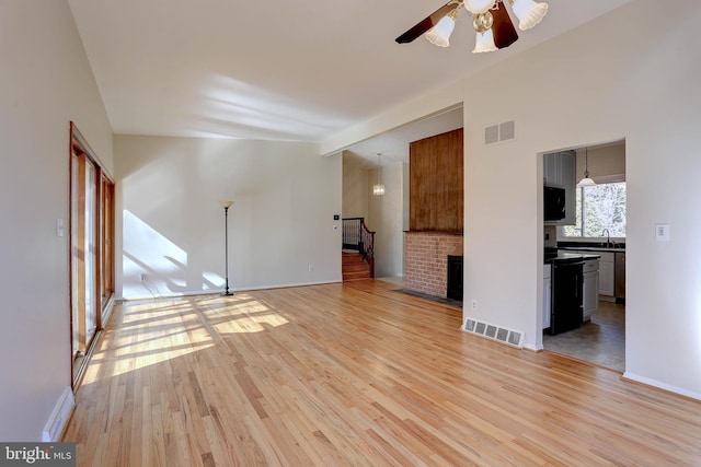 unfurnished living room featuring light wood-type flooring, visible vents, a sink, and stairway