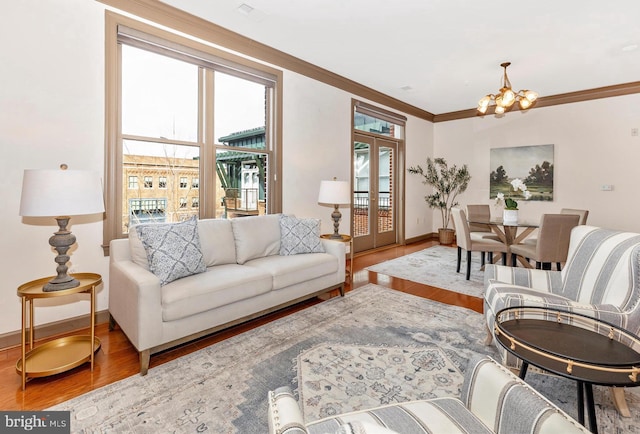 living area featuring baseboards, ornamental molding, wood finished floors, french doors, and a notable chandelier