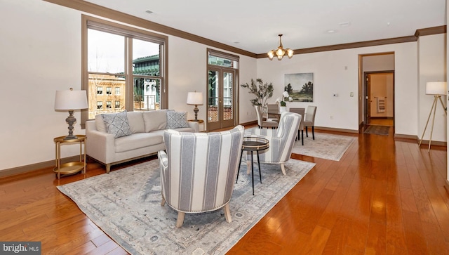 living room with ornamental molding, a notable chandelier, baseboards, and wood finished floors