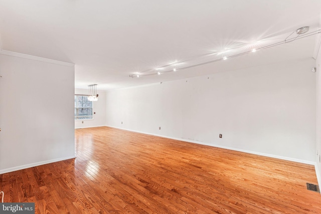 spare room featuring ornamental molding, visible vents, baseboards, and wood finished floors