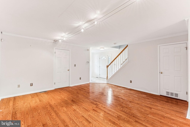 empty room with crown molding, visible vents, light wood-type flooring, baseboards, and stairs