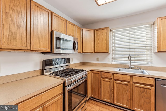 kitchen with appliances with stainless steel finishes, light wood-type flooring, light countertops, and a sink